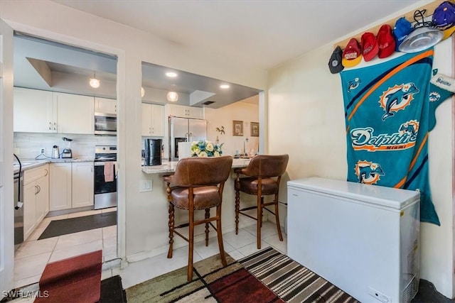 kitchen featuring a breakfast bar area, stainless steel appliances, light tile patterned floors, white cabinetry, and backsplash