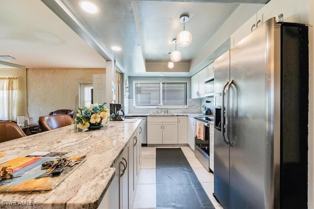 kitchen with hanging light fixtures, a kitchen bar, a tray ceiling, white cabinets, and appliances with stainless steel finishes