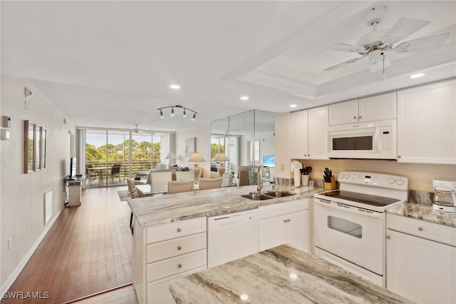kitchen with a sink, open floor plan, wood finished floors, white appliances, and a peninsula