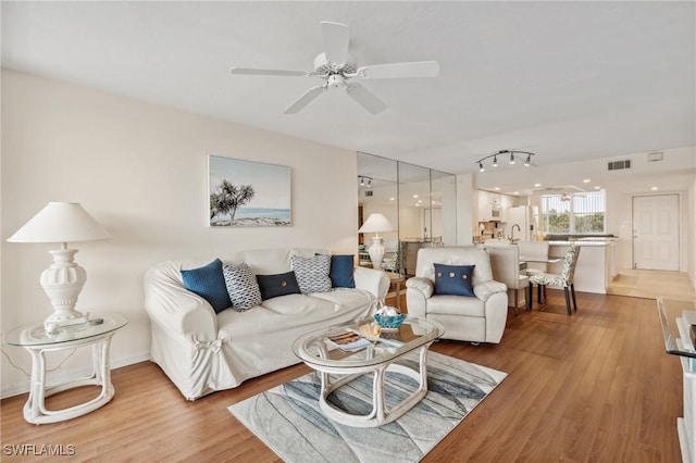 living room with baseboards, wood finished floors, visible vents, and ceiling fan