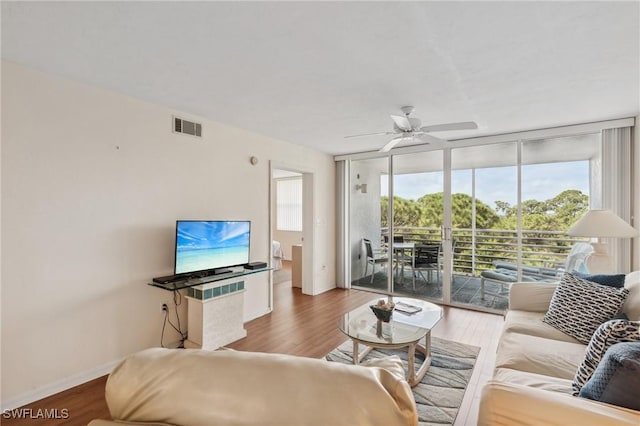 living room with visible vents, wood finished floors, a wall of windows, baseboards, and ceiling fan