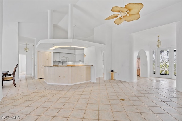 unfurnished living room featuring ceiling fan with notable chandelier, light tile patterned floors, and high vaulted ceiling