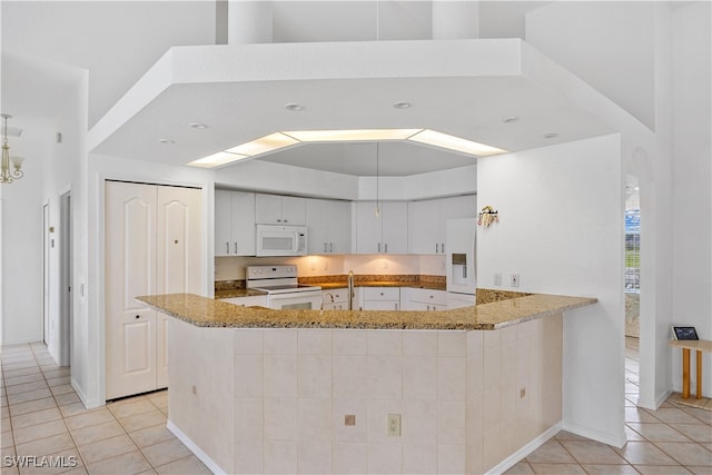 kitchen featuring white appliances, kitchen peninsula, white cabinetry, and stone counters