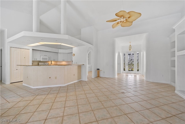 unfurnished living room featuring ceiling fan, light tile patterned flooring, a towering ceiling, and built in shelves