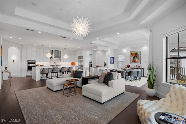 living room with a raised ceiling, sink, dark wood-type flooring, and a notable chandelier