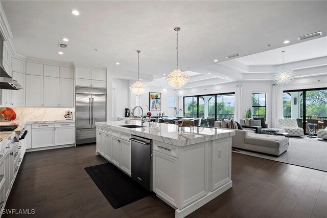 kitchen with sink, white cabinets, stainless steel appliances, light stone countertops, and a center island with sink