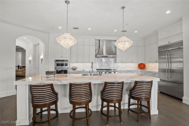 kitchen with a large island with sink, white cabinets, wall chimney range hood, sink, and stainless steel appliances