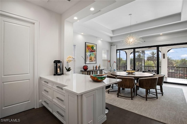 interior space featuring kitchen peninsula, a raised ceiling, pendant lighting, dark hardwood / wood-style floors, and white cabinetry