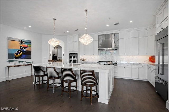 kitchen featuring appliances with stainless steel finishes, a large island, hanging light fixtures, and wall chimney range hood