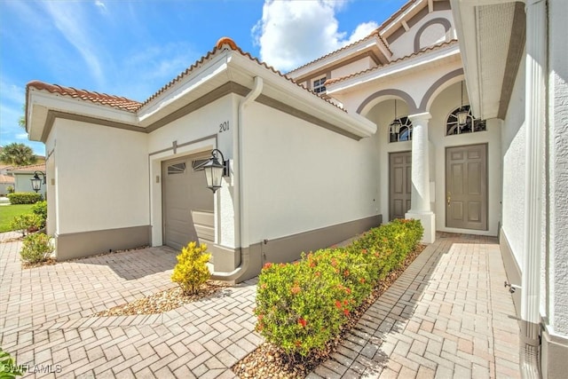 view of exterior entry featuring decorative driveway, a tile roof, an attached garage, and stucco siding