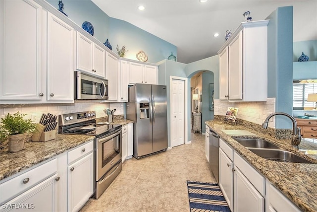 kitchen with a sink, light stone counters, stainless steel appliances, arched walkways, and white cabinets