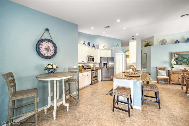 kitchen featuring visible vents, a kitchen bar, light stone counters, appliances with stainless steel finishes, and white cabinetry