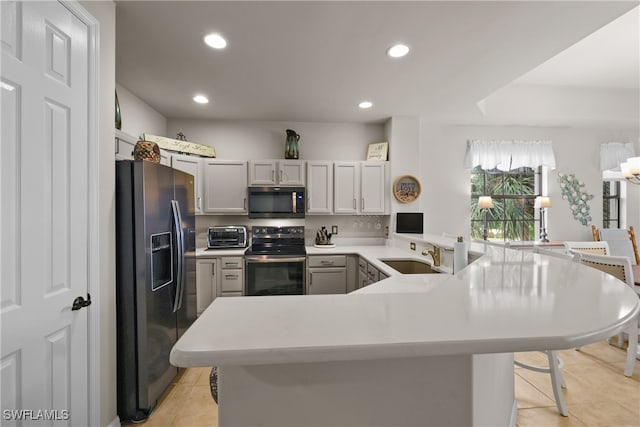 kitchen featuring sink, kitchen peninsula, a kitchen bar, light tile patterned flooring, and appliances with stainless steel finishes