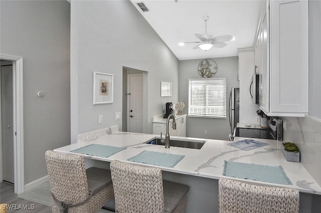 kitchen with white cabinets, kitchen peninsula, stainless steel appliances, ceiling fan, and sink