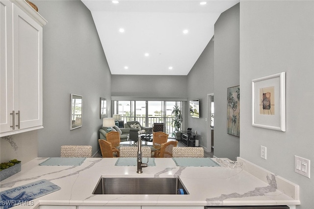 kitchen featuring white cabinets, sink, light stone counters, and high vaulted ceiling