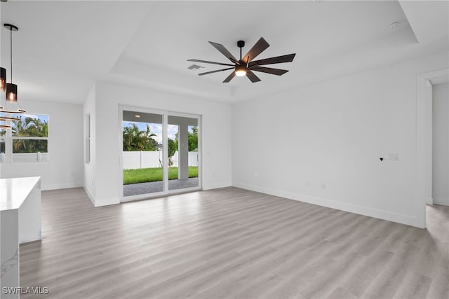 unfurnished living room with light hardwood / wood-style floors, a raised ceiling, plenty of natural light, and ceiling fan