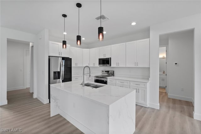 kitchen with light stone countertops, light wood-type flooring, stainless steel appliances, a kitchen island with sink, and white cabinetry