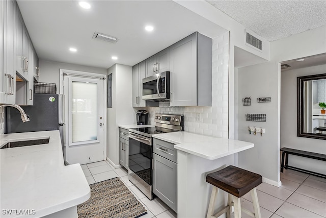 kitchen featuring appliances with stainless steel finishes, sink, light tile patterned floors, and gray cabinets