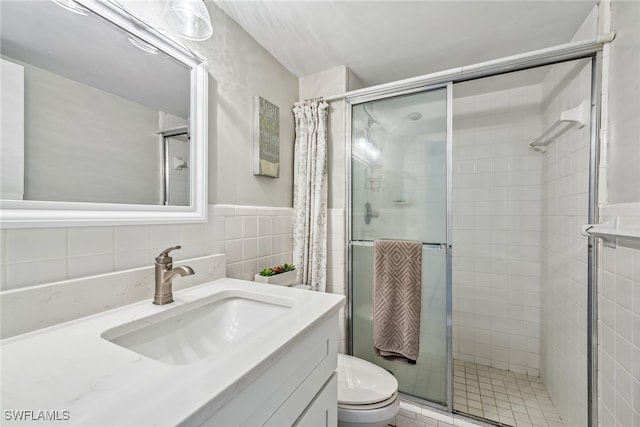 bathroom with tile walls, an enclosed shower, vanity, and toilet