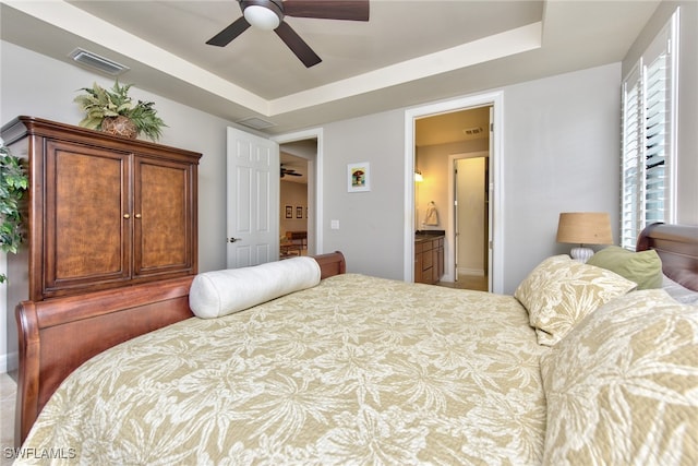 bedroom with ceiling fan, a raised ceiling, and ensuite bathroom