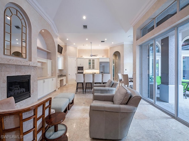 living room with ceiling fan, a tiled fireplace, ornamental molding, and built in shelves