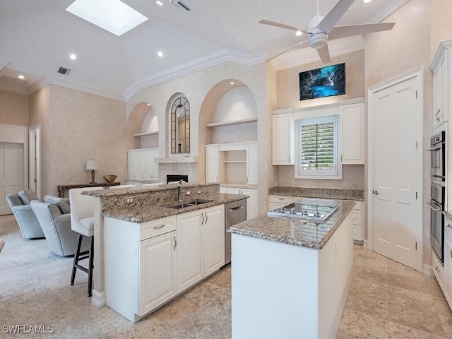 kitchen featuring appliances with stainless steel finishes, white cabinetry, built in shelves, and an island with sink