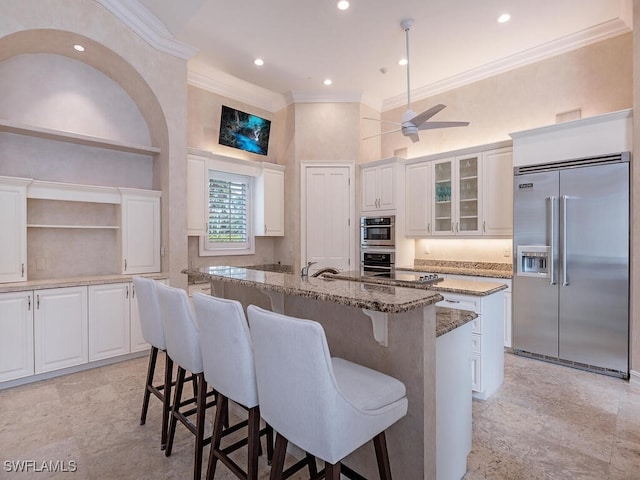 kitchen featuring an island with sink, white cabinetry, stone counters, appliances with stainless steel finishes, and a towering ceiling