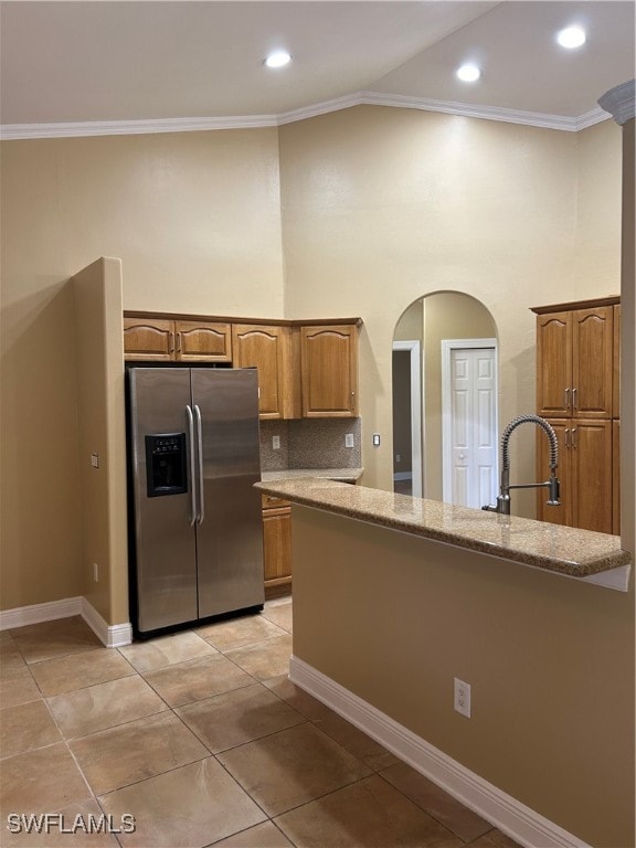 kitchen with sink, ornamental molding, light tile patterned flooring, light stone counters, and stainless steel fridge with ice dispenser