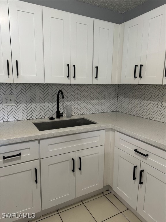 kitchen featuring sink, a textured ceiling, white cabinetry, decorative backsplash, and light tile patterned floors