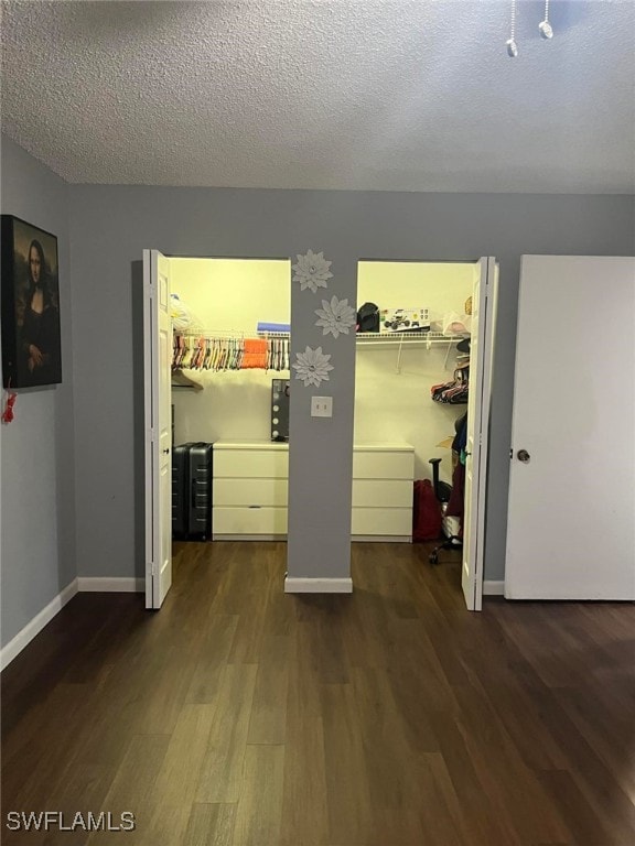 unfurnished bedroom featuring a closet, a textured ceiling, a walk in closet, and dark hardwood / wood-style flooring