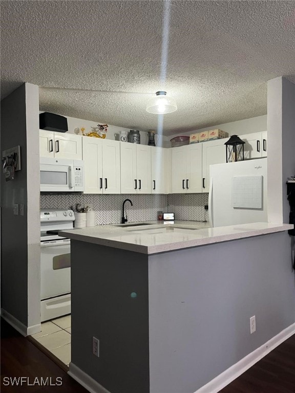 kitchen with decorative backsplash, kitchen peninsula, sink, white cabinets, and white appliances