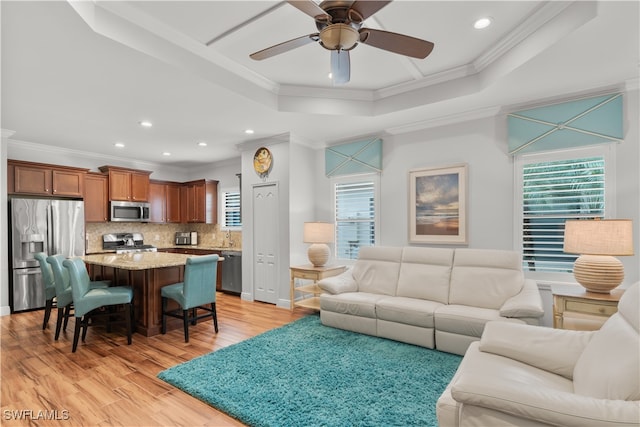 living room featuring ornamental molding, light hardwood / wood-style floors, ceiling fan, and a raised ceiling