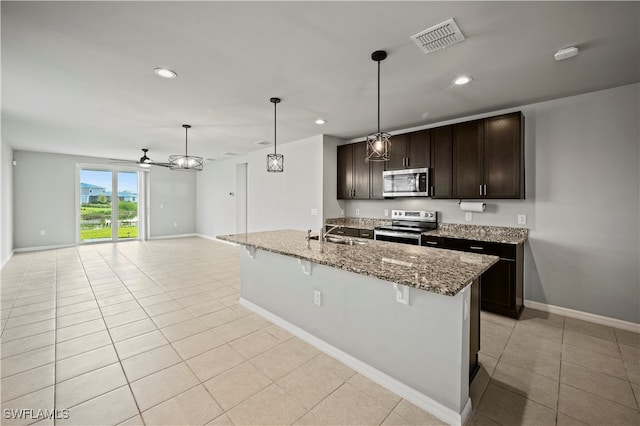 kitchen featuring light stone counters, decorative light fixtures, appliances with stainless steel finishes, and dark brown cabinetry