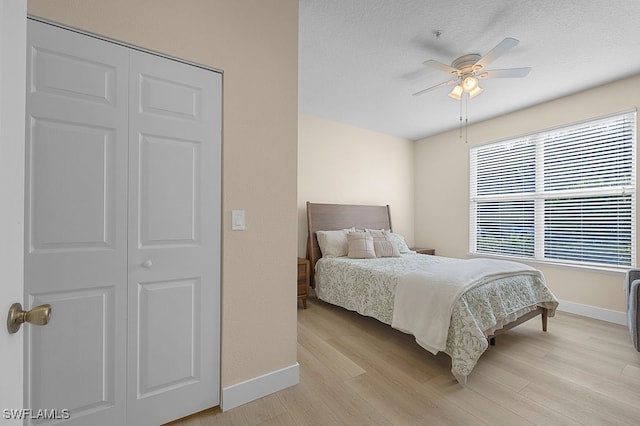 bedroom with a textured ceiling, light hardwood / wood-style floors, ceiling fan, and a closet