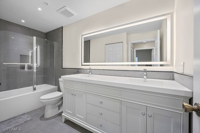 full bathroom featuring vanity, a textured ceiling, tiled shower / bath combo, toilet, and tile patterned floors