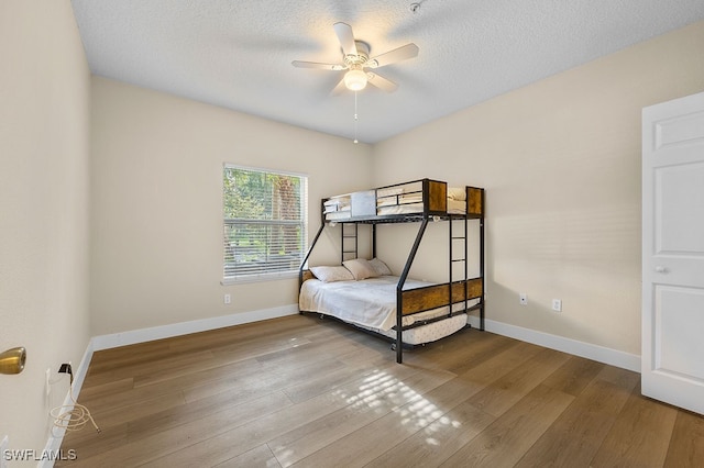 bedroom with a textured ceiling, wood-type flooring, and ceiling fan