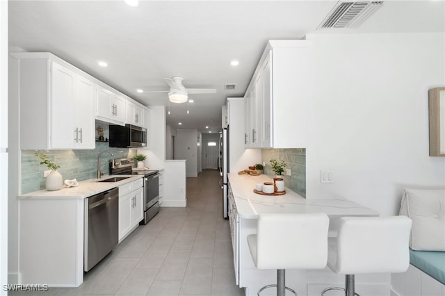 kitchen with light stone counters, white cabinets, tasteful backsplash, appliances with stainless steel finishes, and a breakfast bar