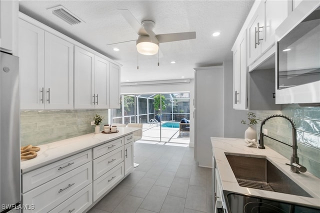 kitchen with white cabinetry, ceiling fan, appliances with stainless steel finishes, and light stone counters