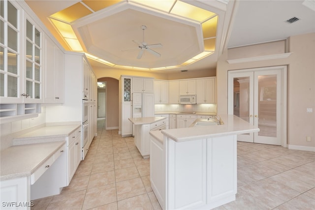 kitchen featuring a tray ceiling, a kitchen island with sink, ceiling fan, and white cabinets