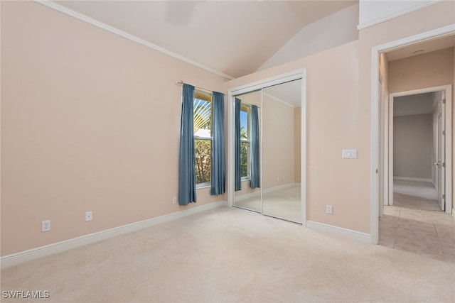 unfurnished bedroom featuring lofted ceiling, ornamental molding, light carpet, and a closet