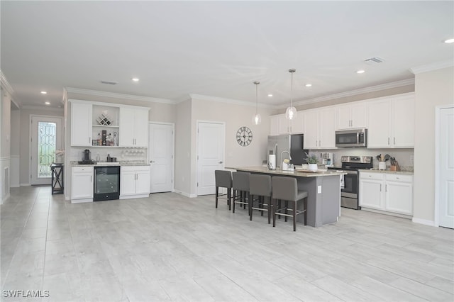 kitchen featuring pendant lighting, stainless steel appliances, white cabinets, and a center island with sink