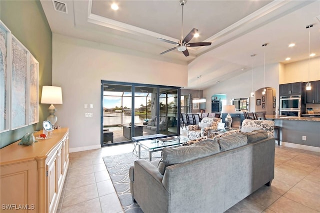 tiled living room with crown molding, a tray ceiling, ceiling fan, and high vaulted ceiling