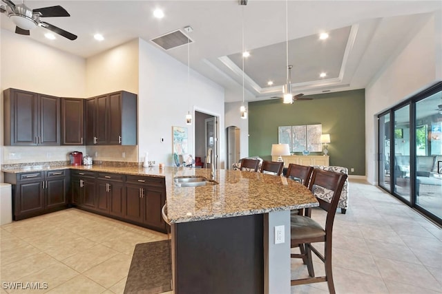 kitchen with ceiling fan, a raised ceiling, sink, decorative light fixtures, and a breakfast bar area