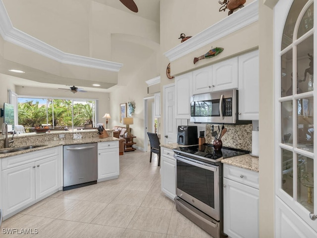 kitchen with a high ceiling, light stone countertops, white cabinetry, light tile patterned floors, and appliances with stainless steel finishes