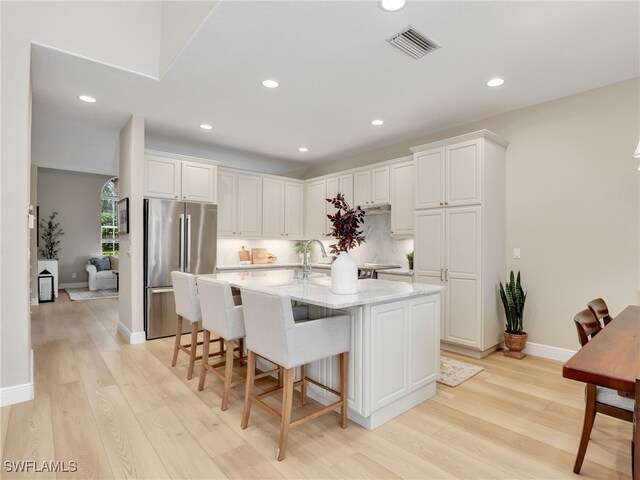 kitchen featuring white cabinets, an island with sink, light hardwood / wood-style floors, and high end refrigerator