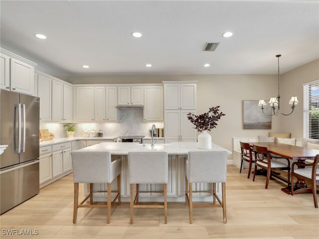 kitchen with light hardwood / wood-style flooring, a chandelier, a center island with sink, and stainless steel fridge