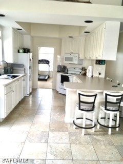 kitchen with a kitchen breakfast bar, white appliances, white cabinetry, and kitchen peninsula