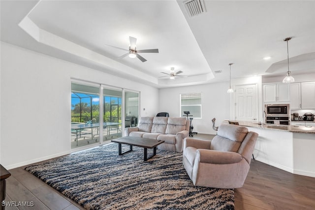 living room featuring ceiling fan, a tray ceiling, and dark hardwood / wood-style floors