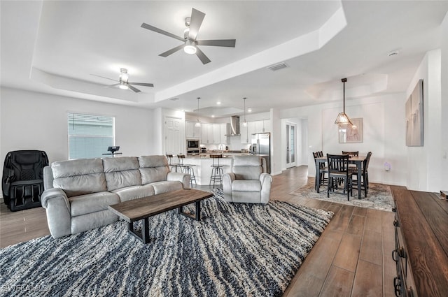 living room featuring ceiling fan, a tray ceiling, and dark wood-type flooring