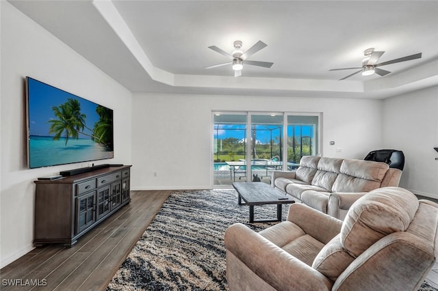 living room with ceiling fan, a raised ceiling, and dark hardwood / wood-style floors